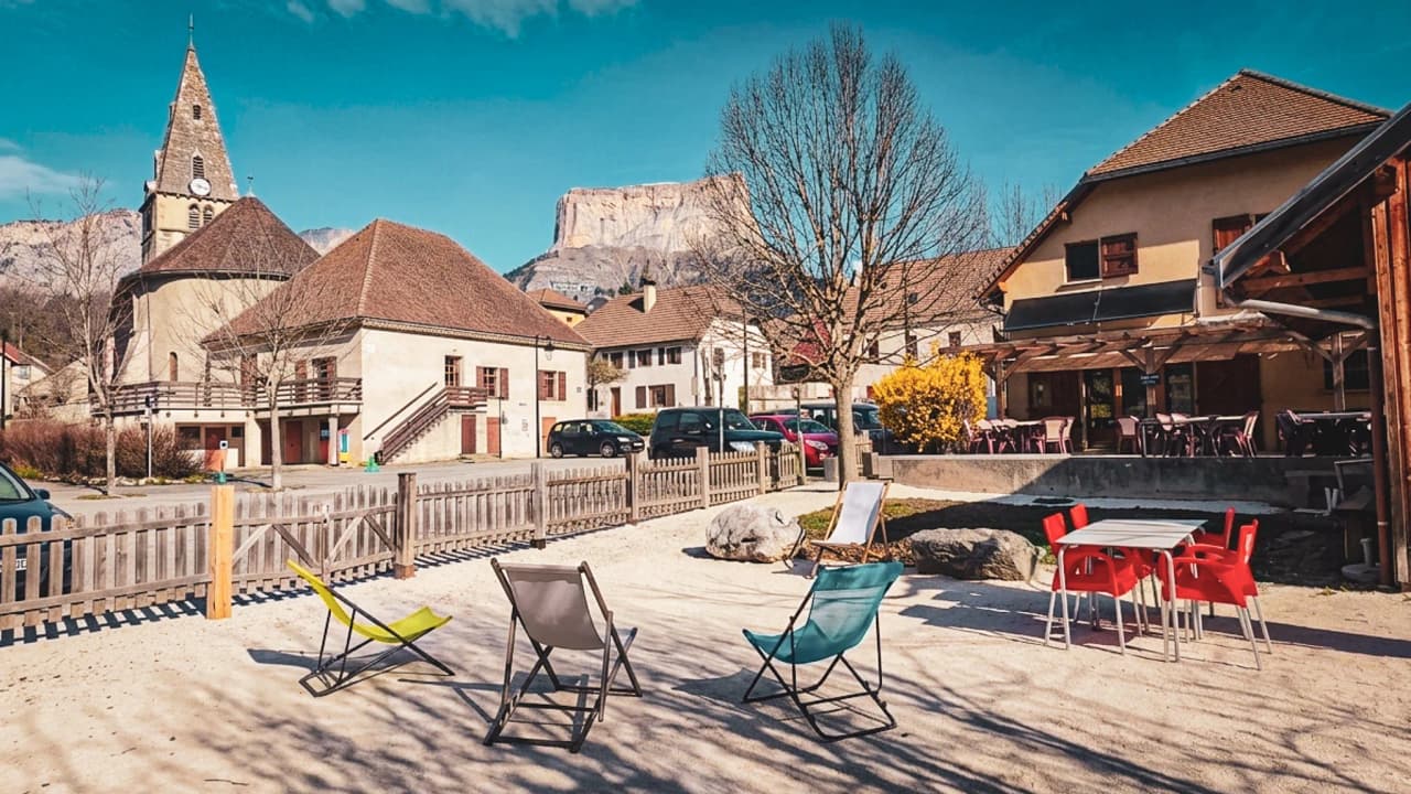 Een charmant dorpsplein met kleurrijke stoelen, majestueuze bergen en blauwe luchten.