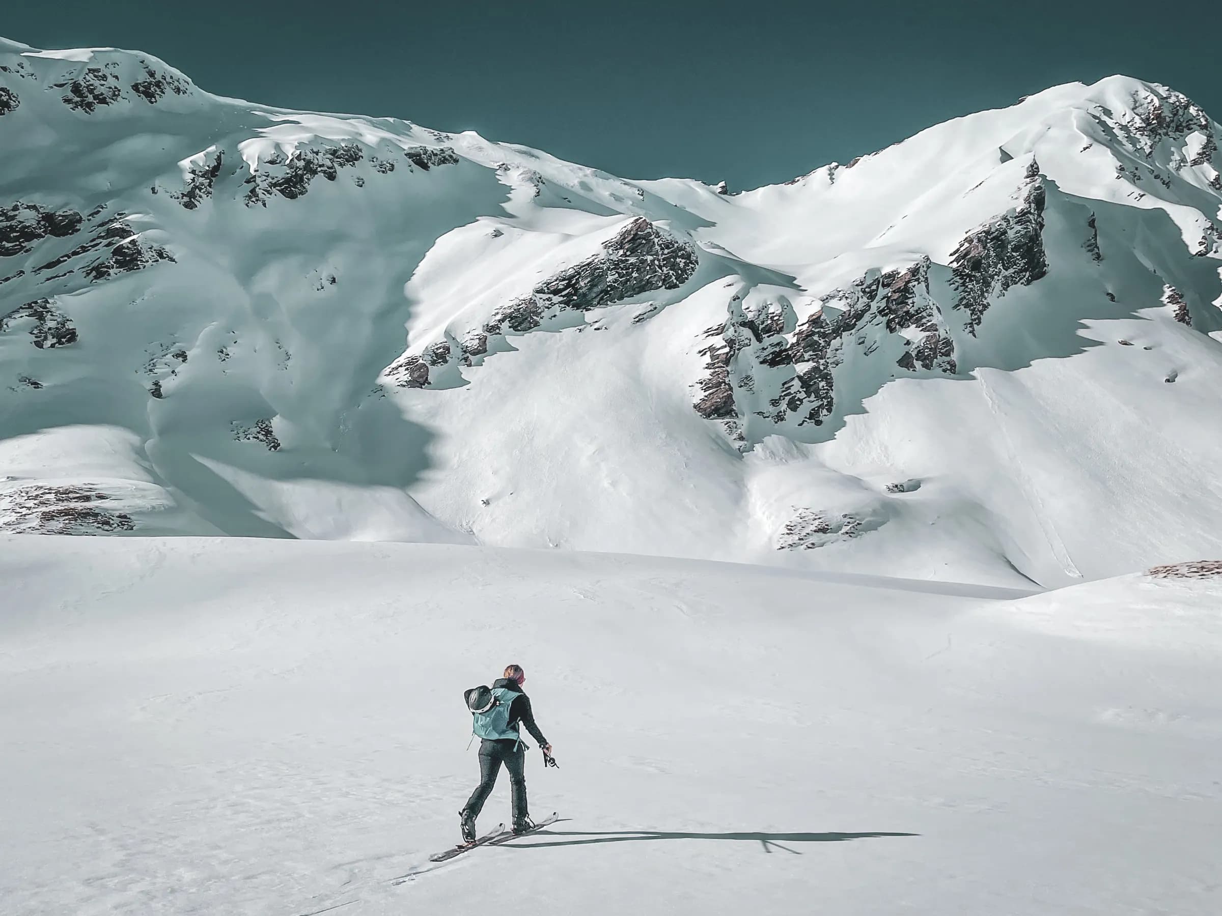 A lone skier crosses a vast landscape of glaciers under an azure sky, inviting adventure.