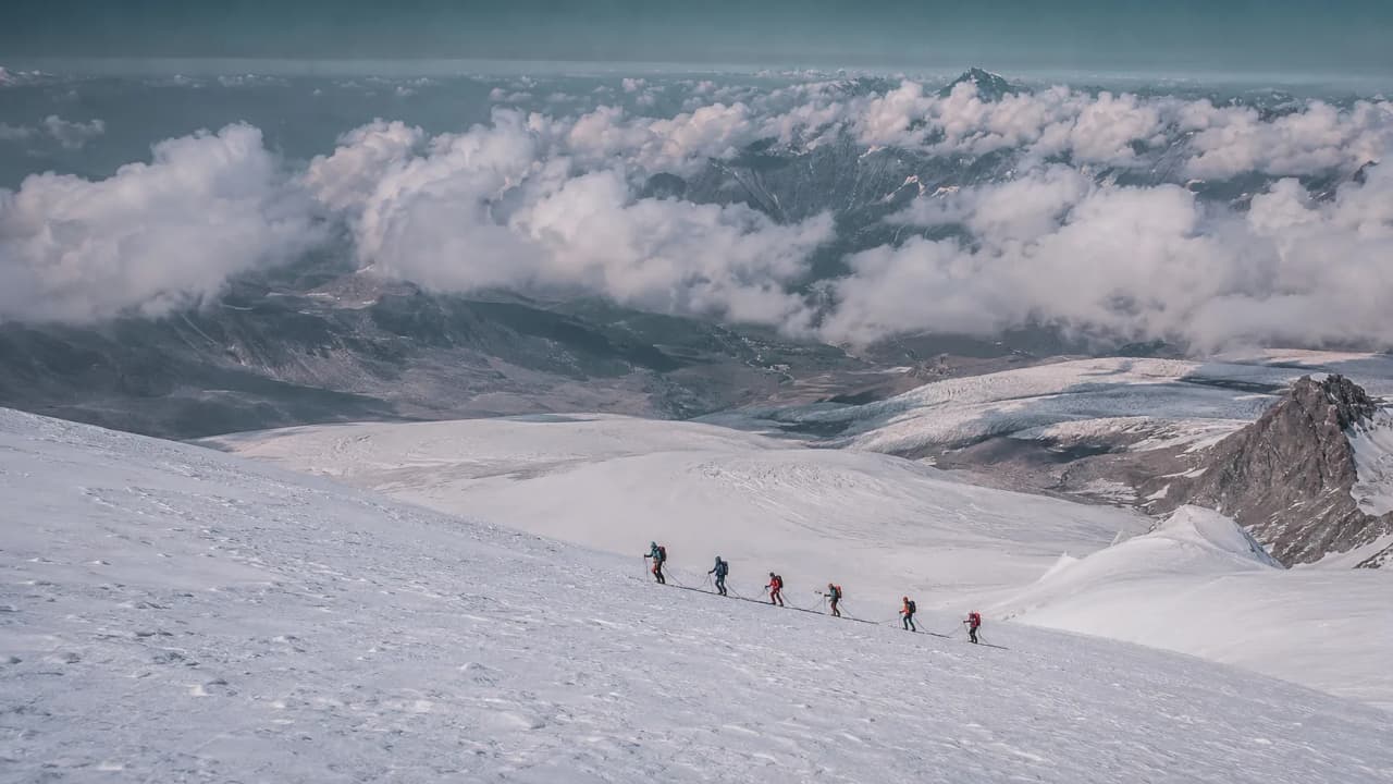 A group of mountaineers climbing the Breithorn, against a majestic backdrop of snow and clouds.