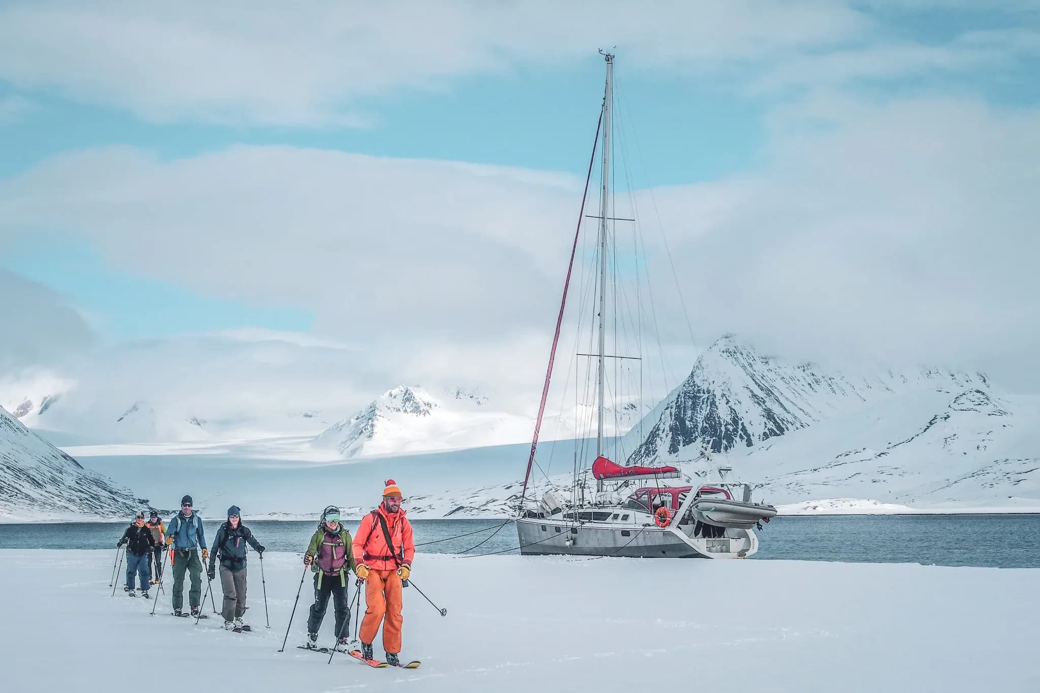 A group of ski-tourers make their way across the snow, with majestic mountains in the background.
