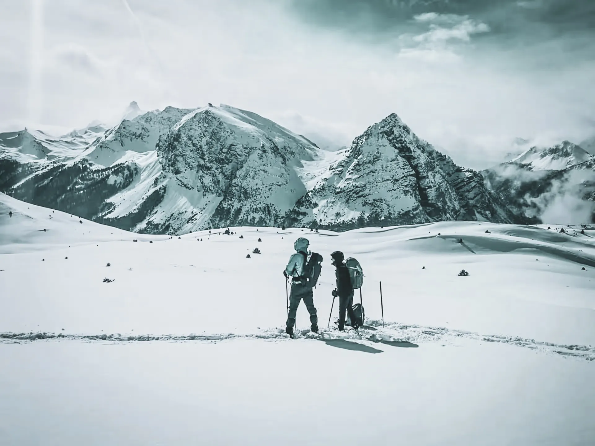 Two hikers on snowshoes on a vast expanse of immaculate snow, facing majestic peaks.