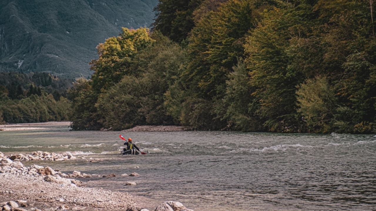 A packraft adventurer glides down an Alpine river surrounded by lush green mountains.