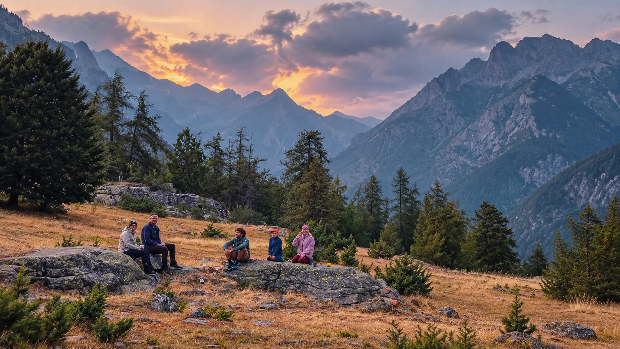 Groupe de randonneurs se reposant sur des rochers, avec des montagnes et un coucher de soleil en toile de fond.