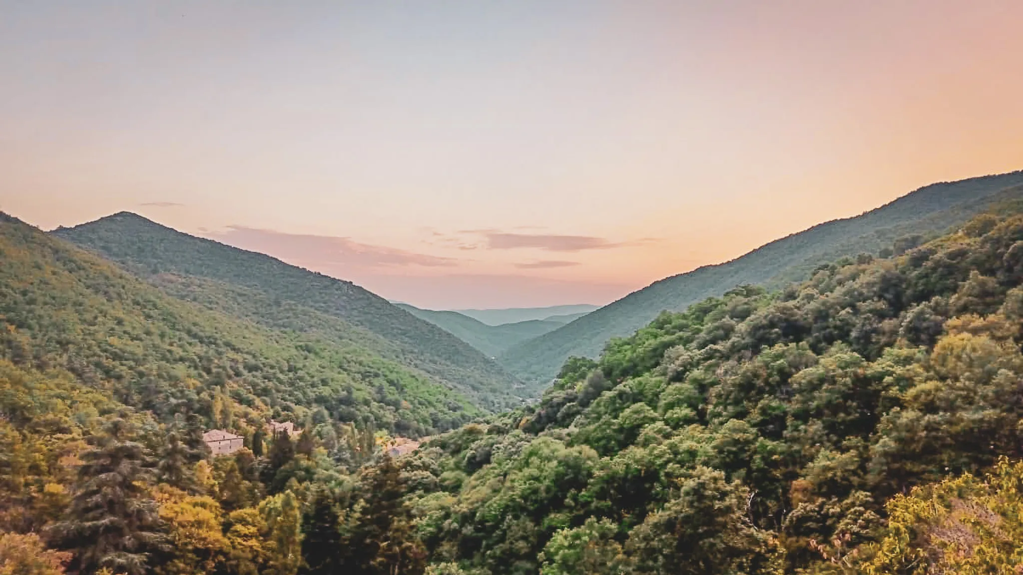 A panoramic view of the Cévennes: lush green hills and a pastel-coloured sky that invite you to get away from it all.