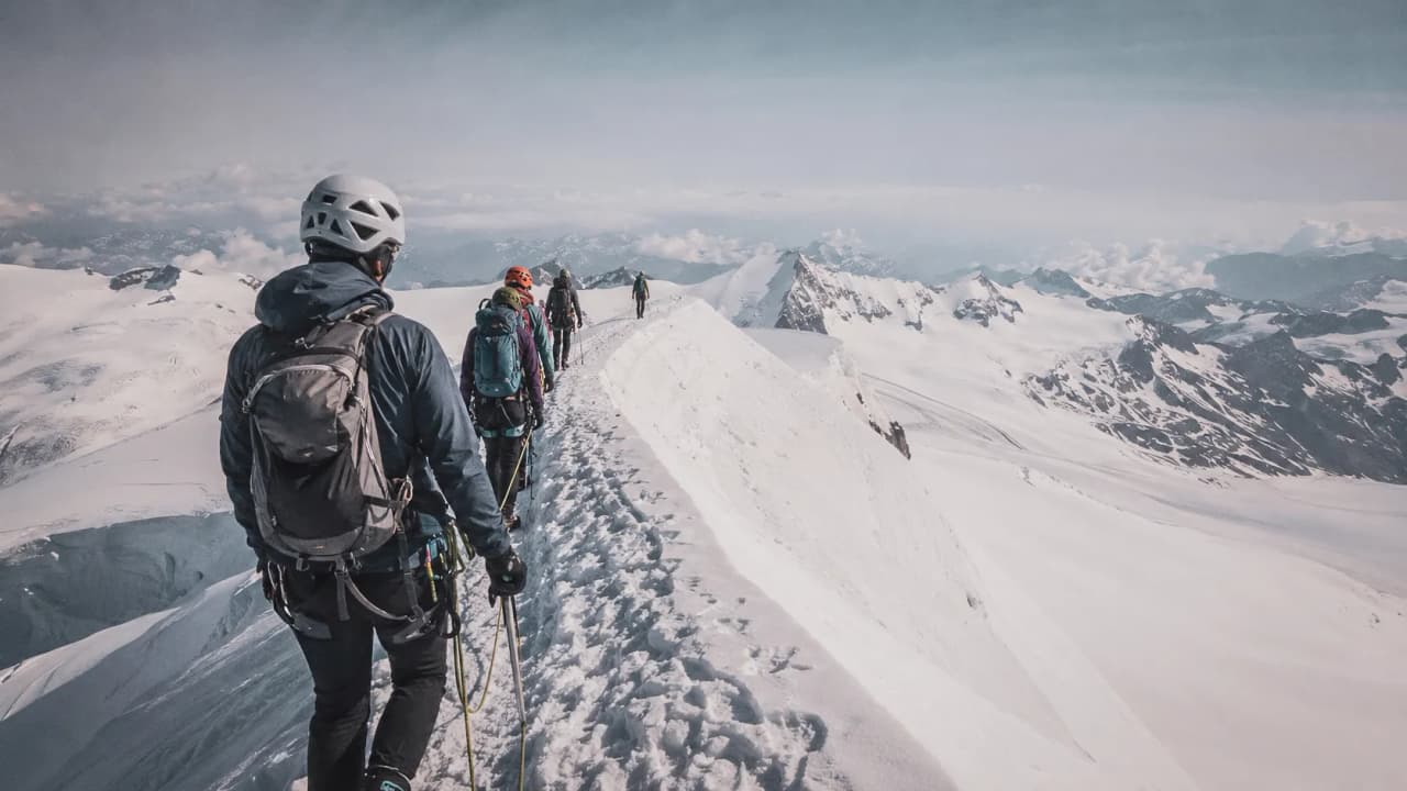 A group of hikers making their way along a snow-covered ridge, with majestic peaks in the background.