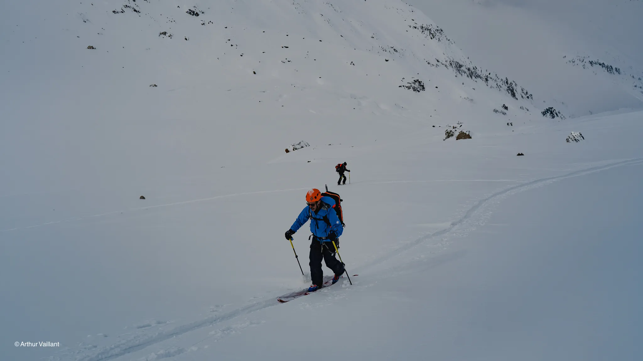 Two skiers are making their way across a vast snow-covered landscape, climbing towards the majestic Alpine peaks.