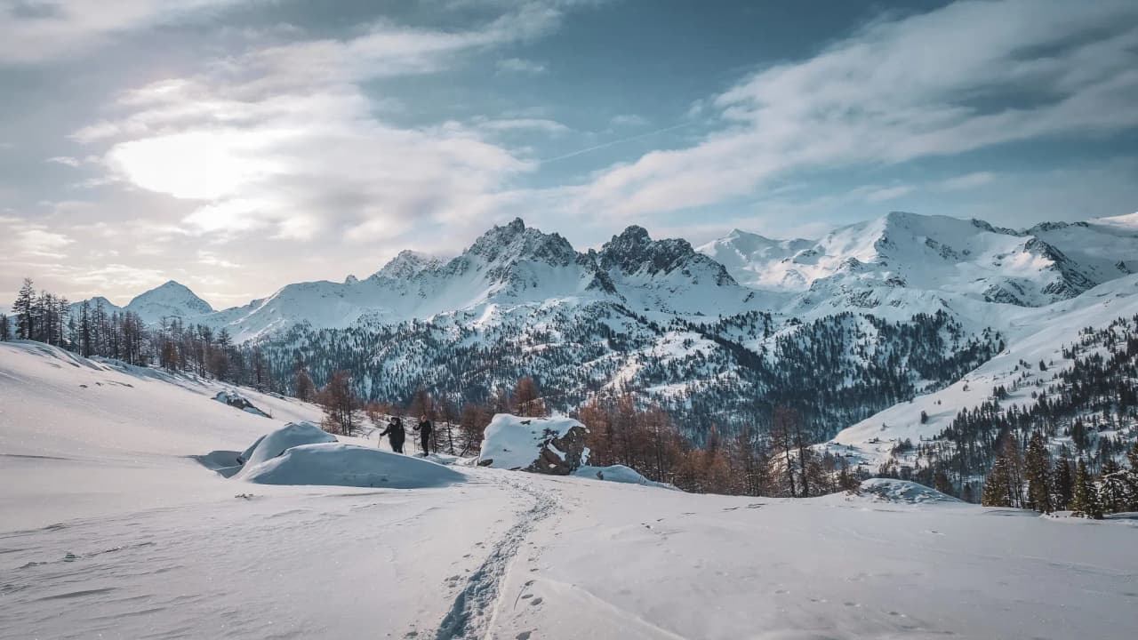 A snow-covered alpine landscape with majestic mountains, and hikers on a peaceful trail.