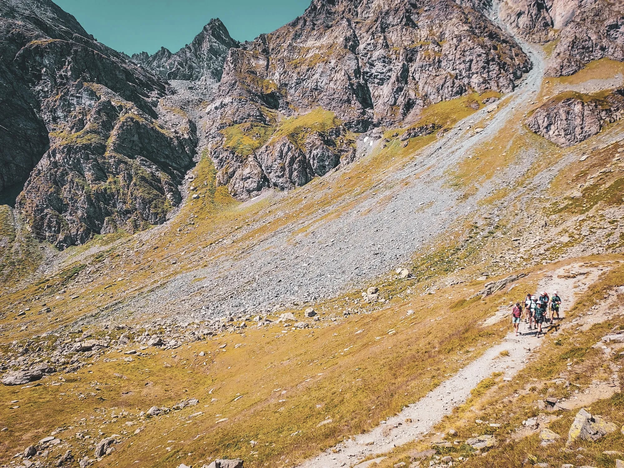 Groupe de randonneurs cheminant sur un sentier alpin, entouré de montagnes majestueuses.