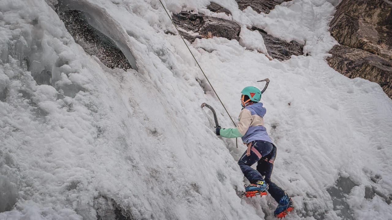 One person climbs an ice wall, surrounded by the immensity of the Alps, a moment of adventure.