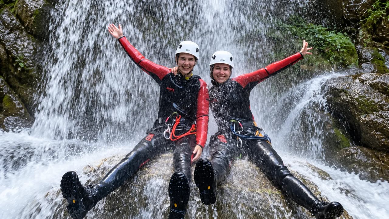 Deux aventurières en tenue de canyoning s'amusent sous une cascade rafraîchissante dans le Vercors.