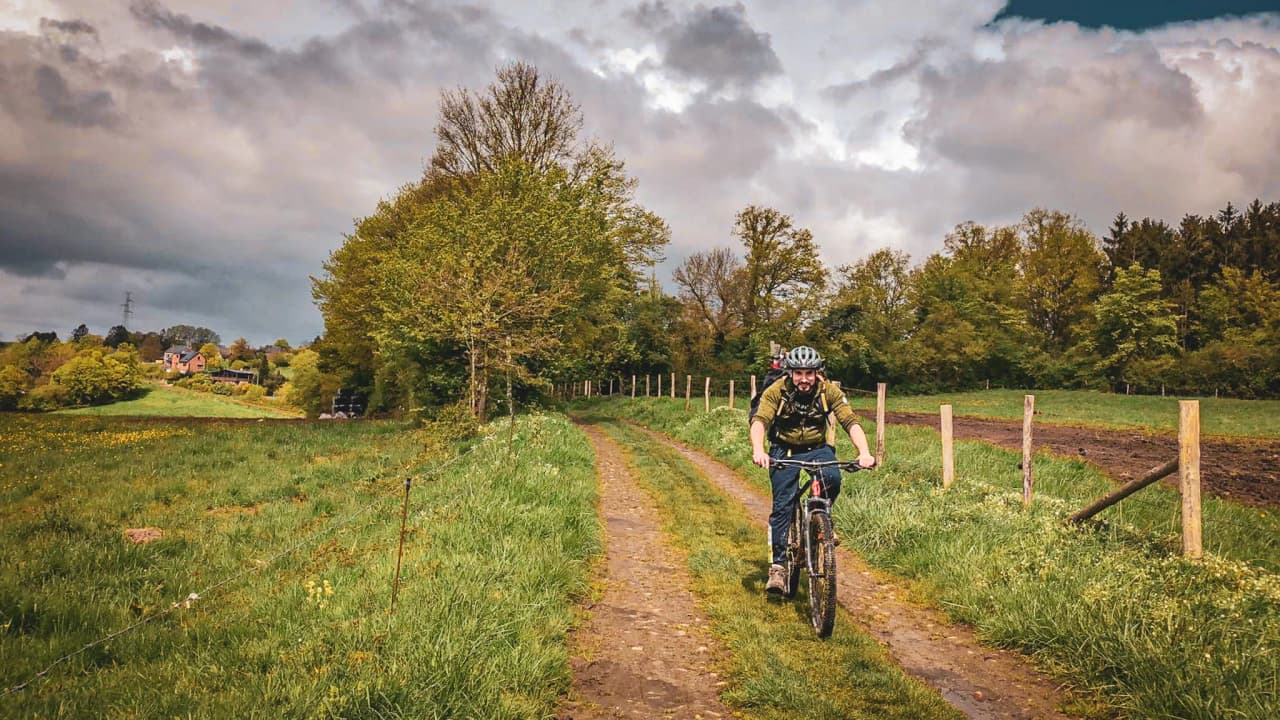 An enthusiastic cyclist pedals along a green road, surrounded by lush forests.