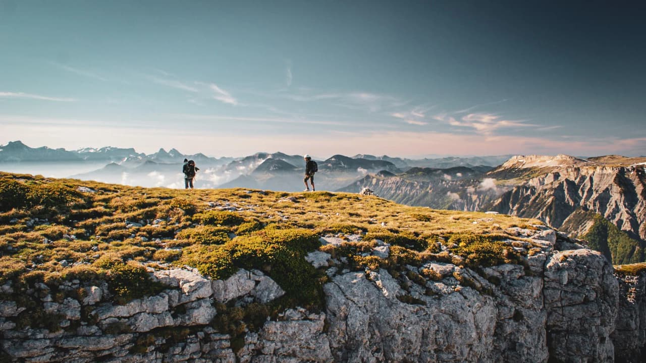 Wandelaars op een groene top, met een spectaculair uitzicht op de omliggende bergen.