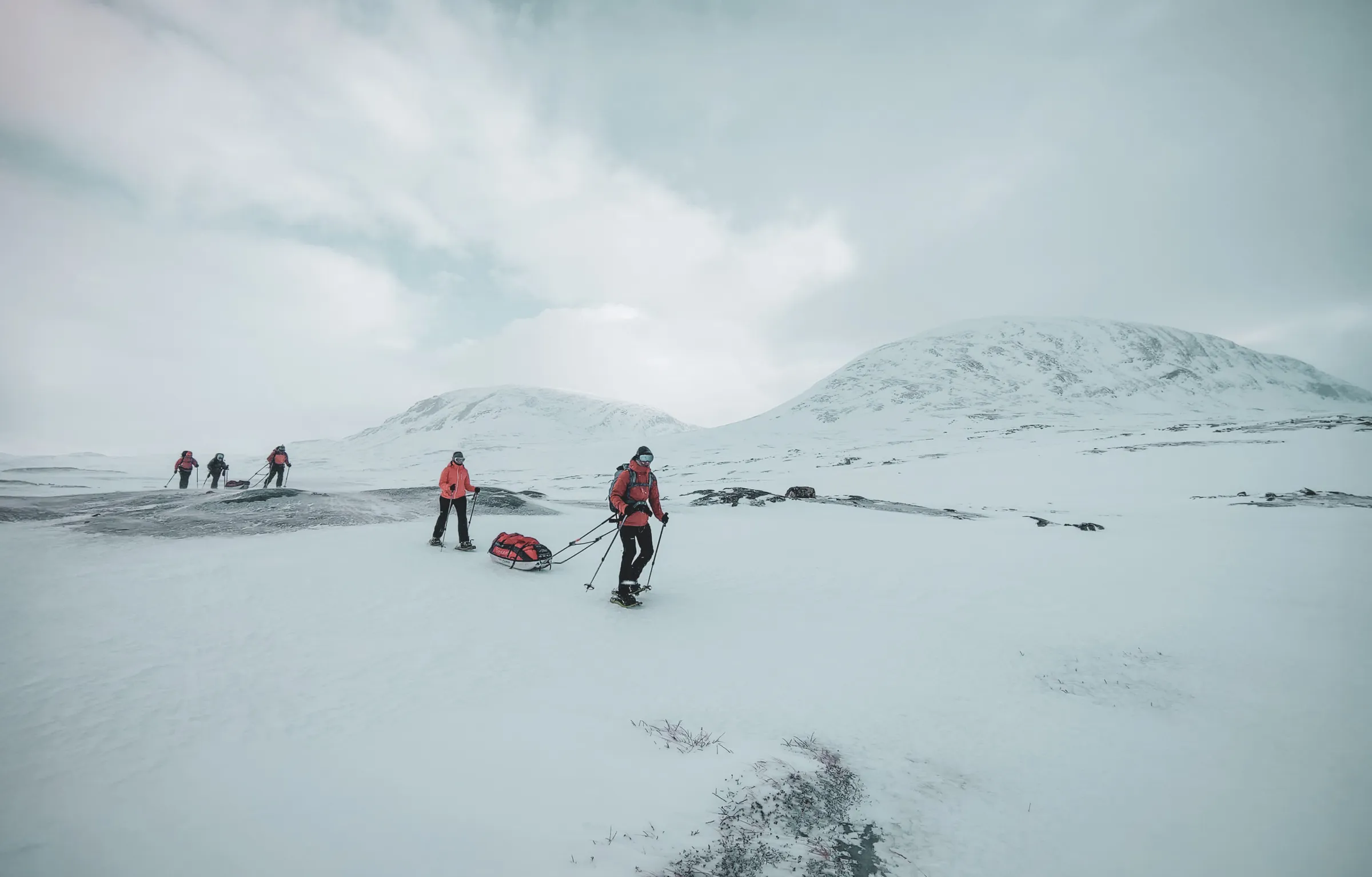Équipe d'expéditions en raquettes sur la neige, sous un ciel chargé au nord du cercle polaire.