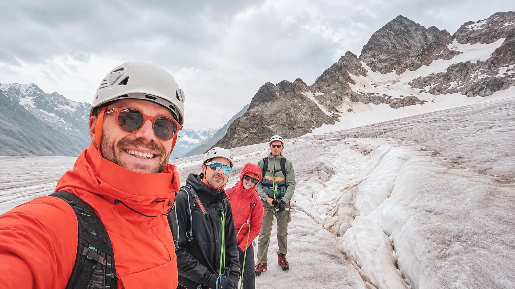 Quatre alpinistes souriants sur un glacier des Écrins, prêts à gravir des sommets majestueux.