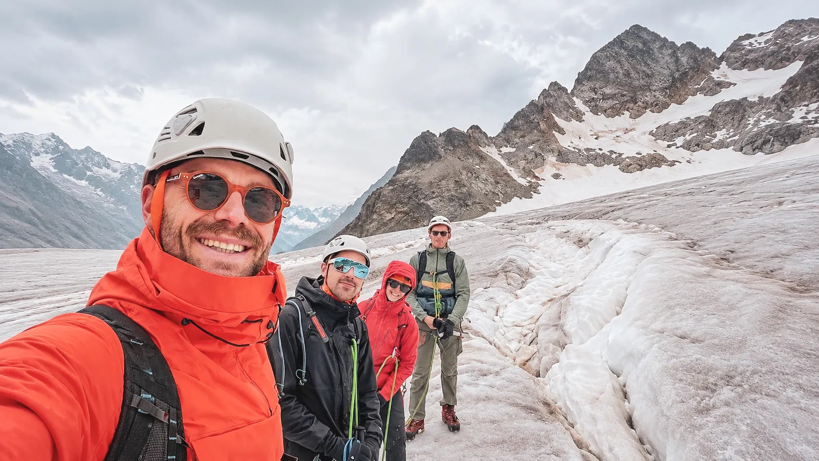 Quatre alpinistes souriants sur un glacier des Écrins, prêts à gravir des sommets majestueux.