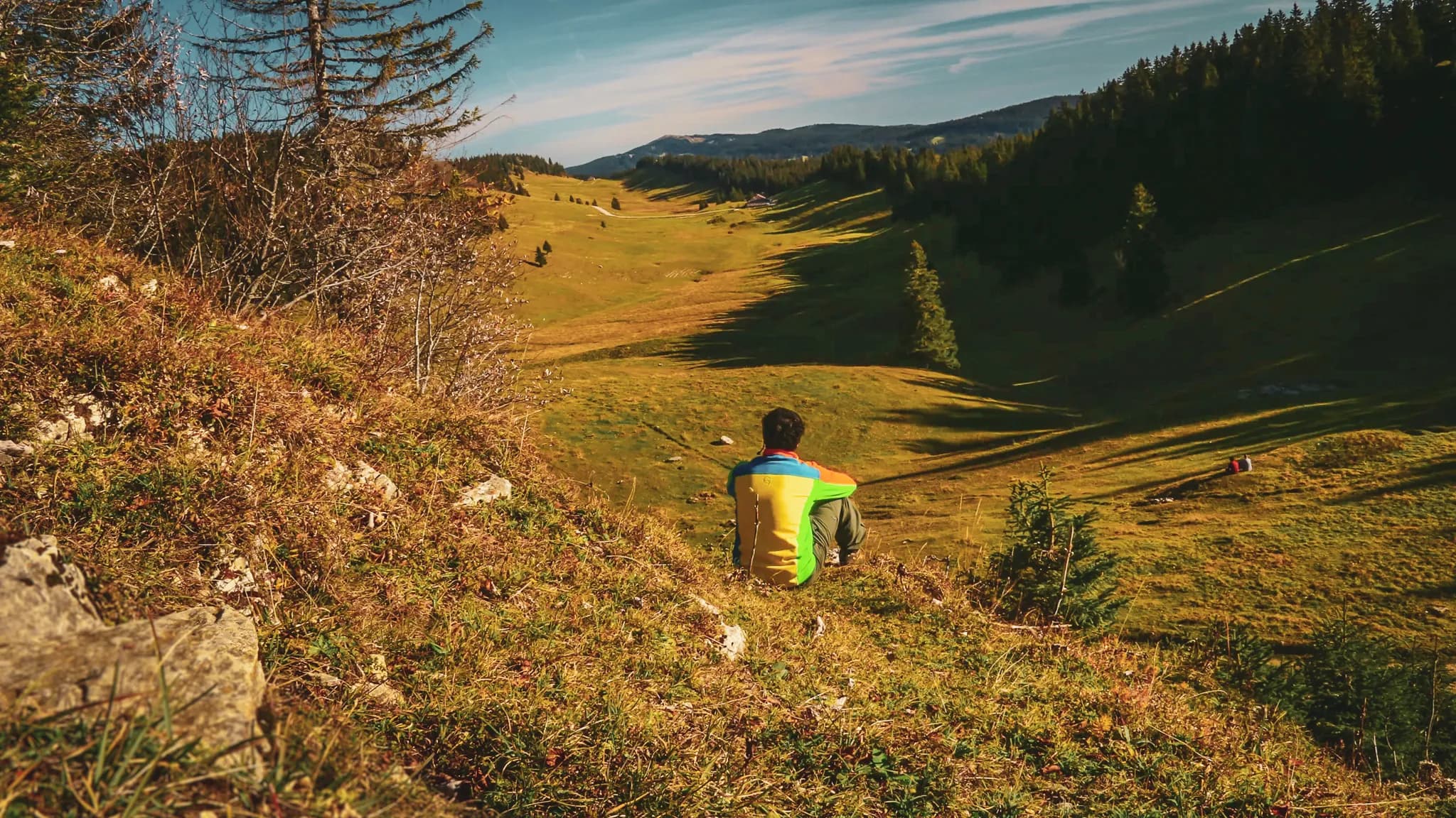 A hiker contemplating a sun-drenched green landscape in the Jura, an invitation to escape.