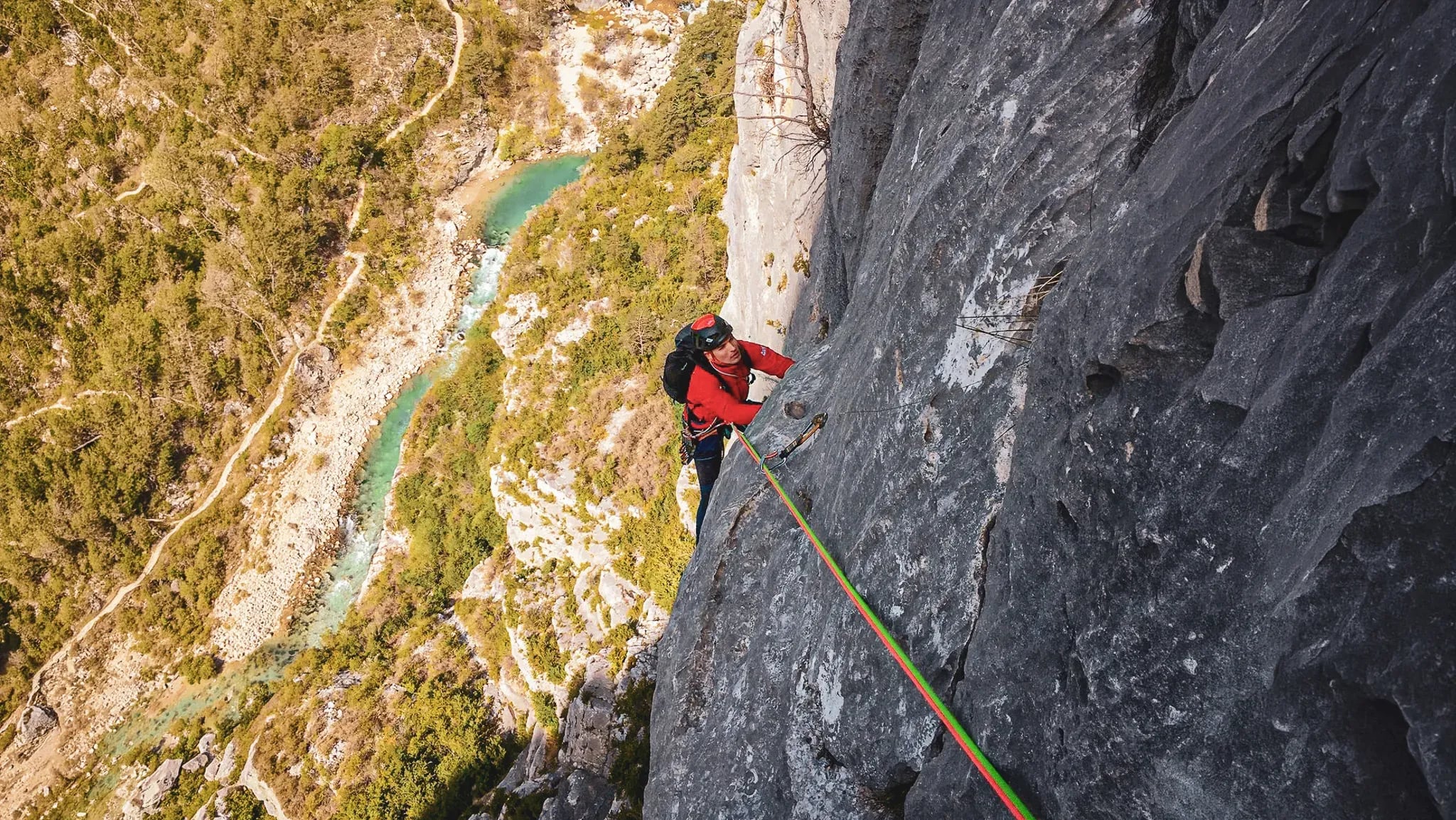 Grimpeur en pleine ascension sur un rocher, surplombant les gorges verdoyantes du Verdon.