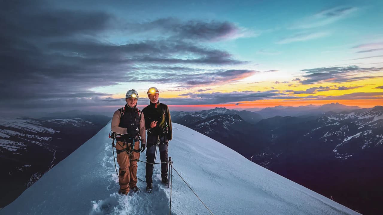 Two mountaineers on the snow-covered summit of Mont Blanc, admiring a spectacular sunset.