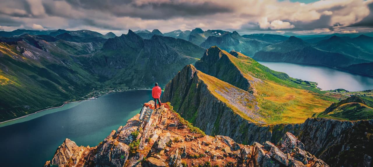 Een wandelaar kijkt uit over majestueuze fjorden en groene bergtoppen op het eiland Senja.