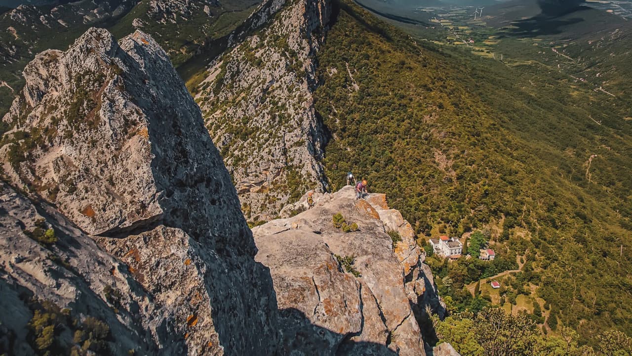 Vue panoramique sur une crête rocheuse avec des grimpeurs, au milieu des Pyrénées verdoyantes.