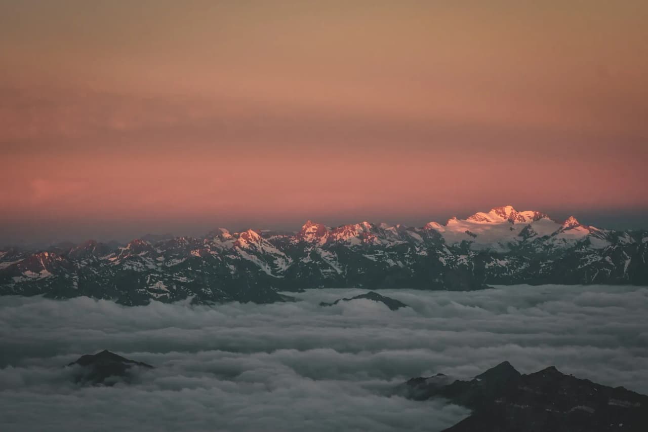 Paysage alpin au coucher du soleil, montagnes enneigées émergeant des nuages.