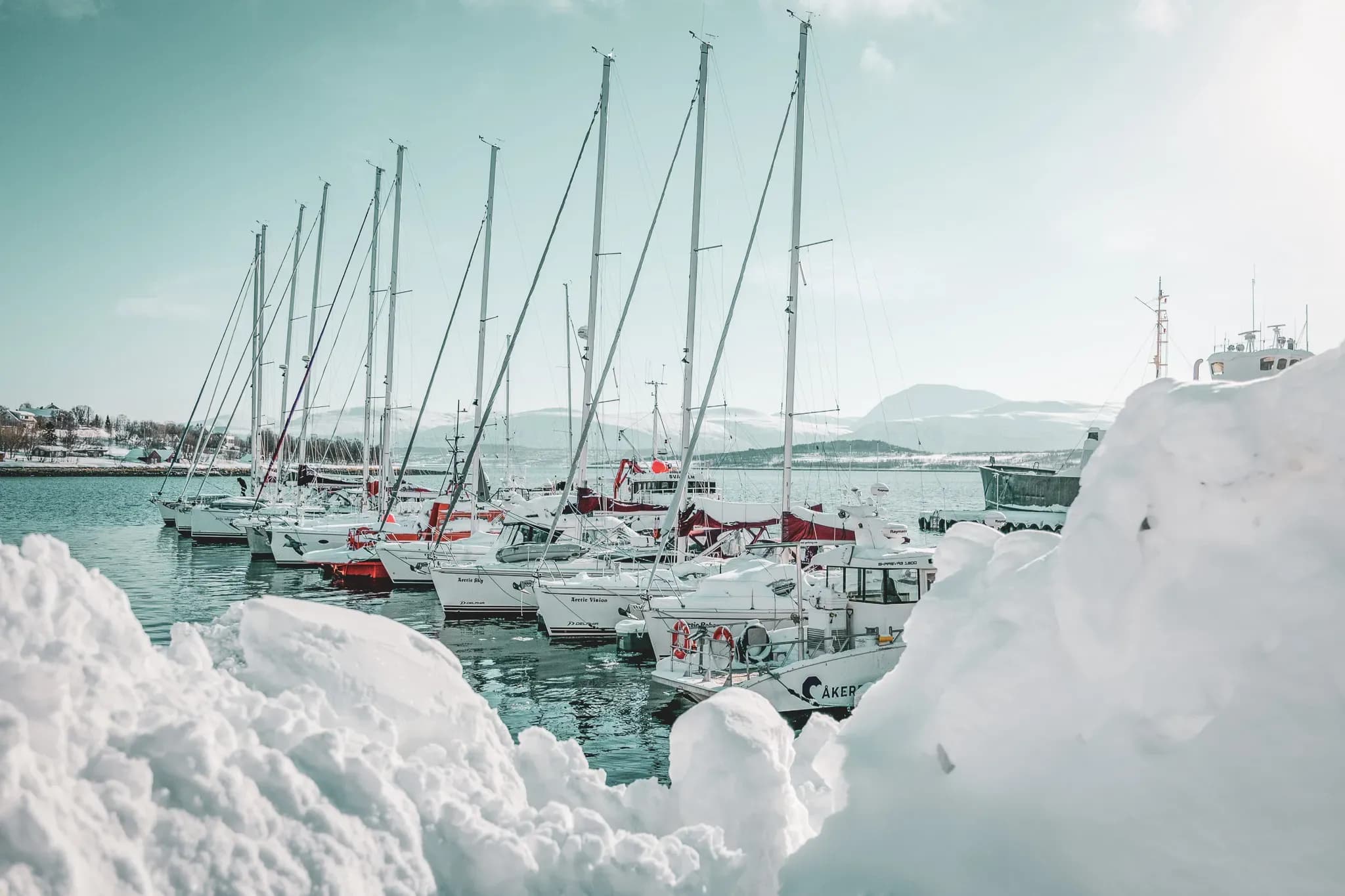 Lyngen Alpine harbour, sailing boats at anchor surrounded by glistening snow. A winter escape.