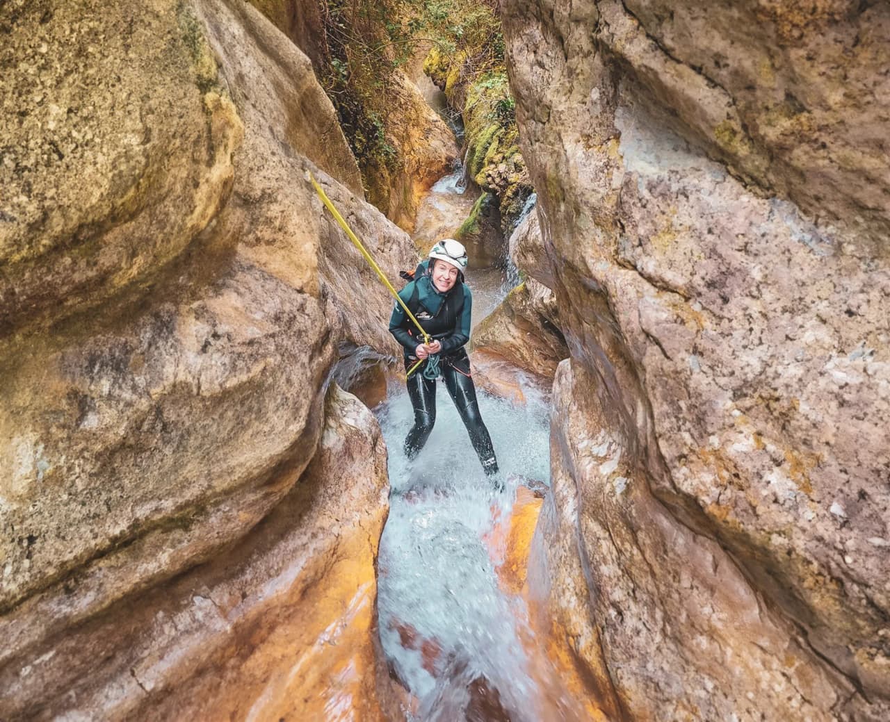Aventurière en canyoning, encadrée par des falaises colorées, s'apprête à descendre dans l'eau turquoise.
