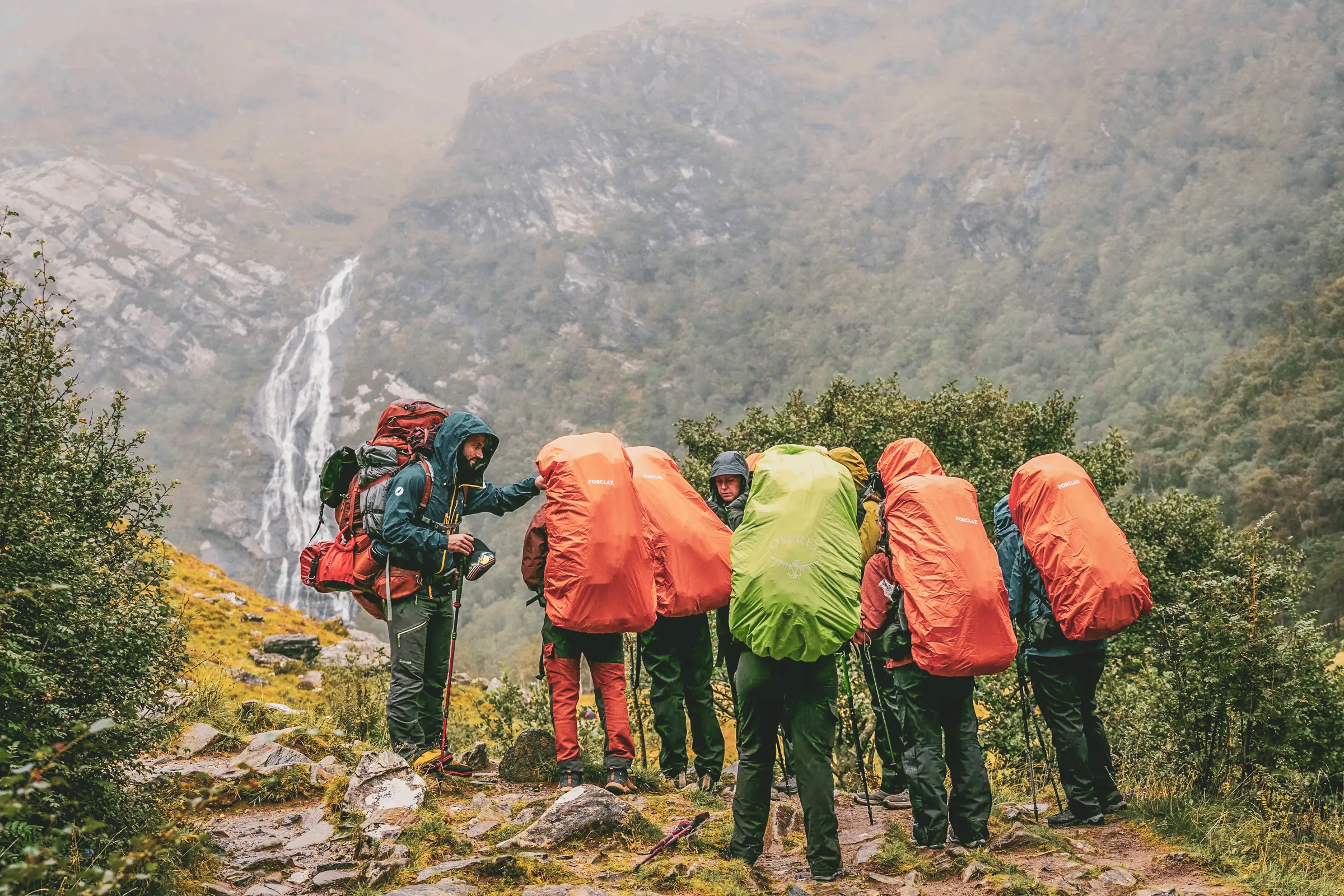 Groep wandelaars in de regen, kleurrijke rugzakken, bewonderen de woeste landschappen van de Highlands.
