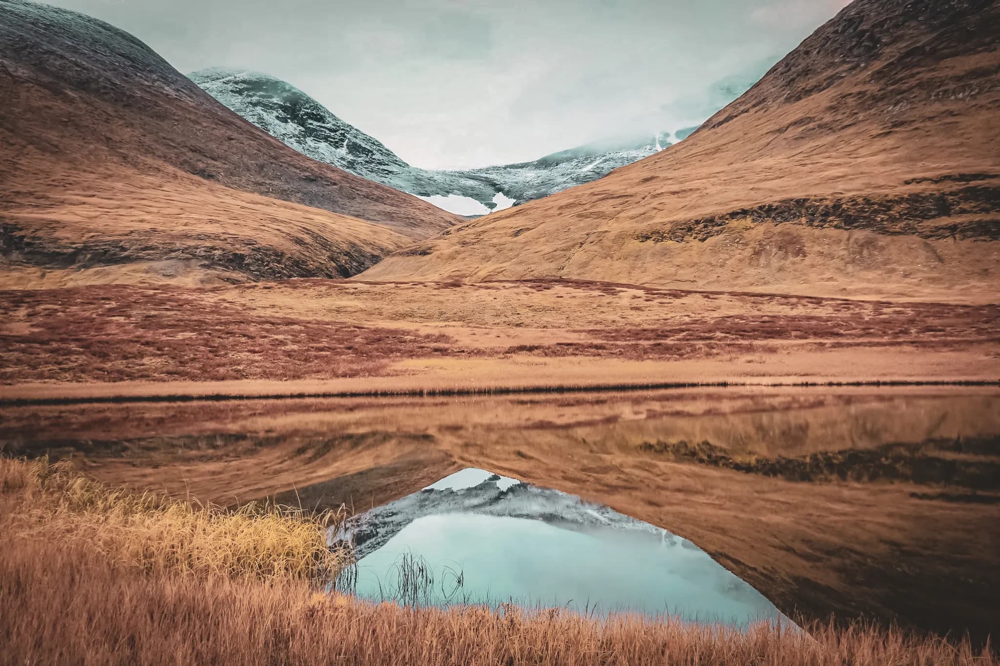 Golden valleys and snow-capped mountains reflected in a calm lake in Swedish Lapland.
