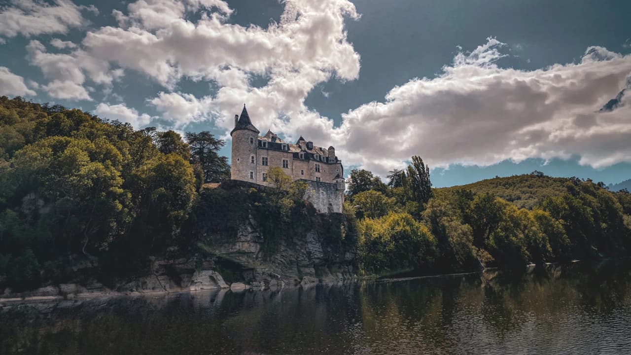Château majestueux surplombant la Dordogne, entouré de verdure, idéal pour une aventure en canoë.