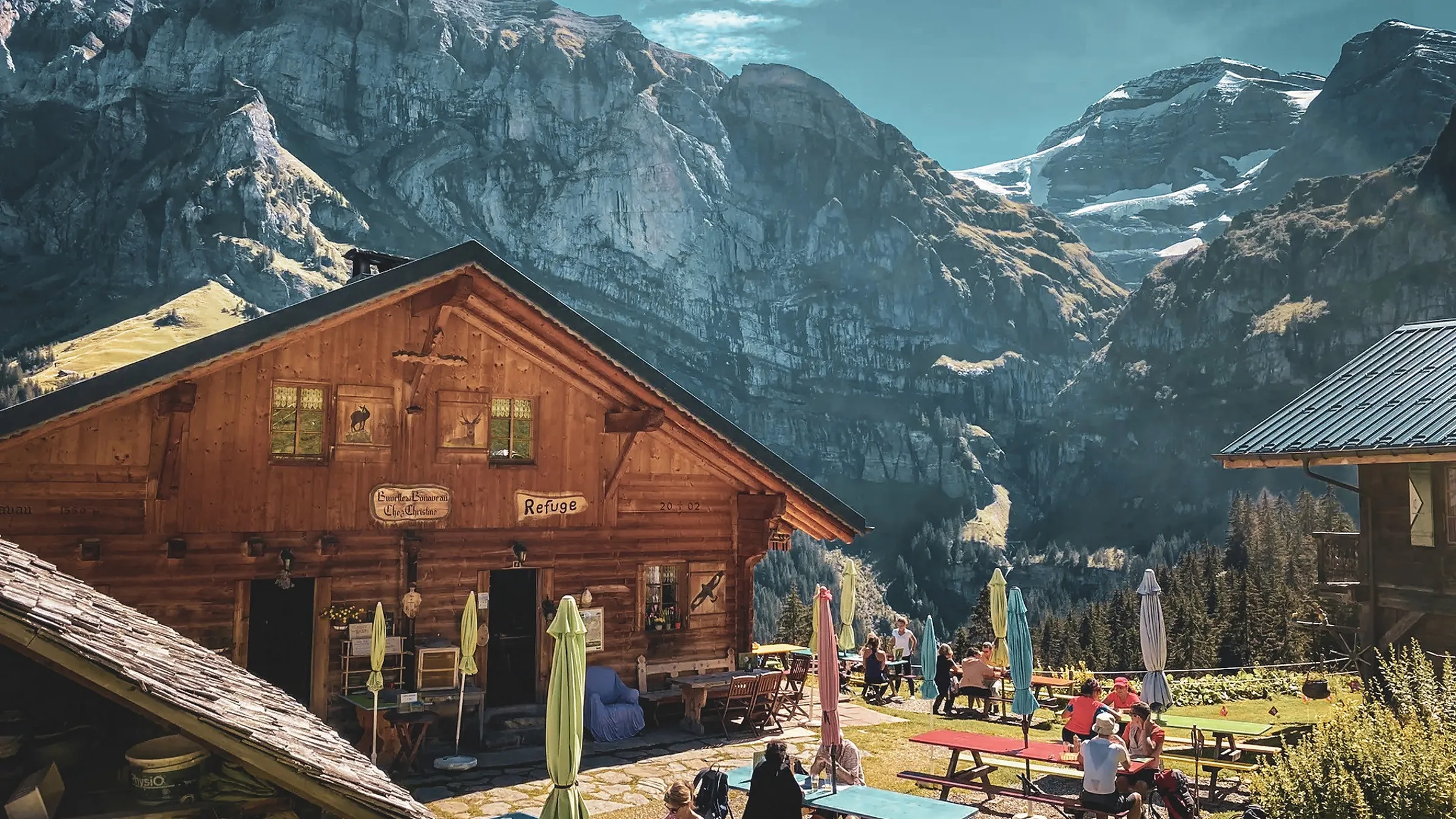 Refuge en bois pittoresque entouré de montagnes, avec des randonneurs profitant du paysage alpin.