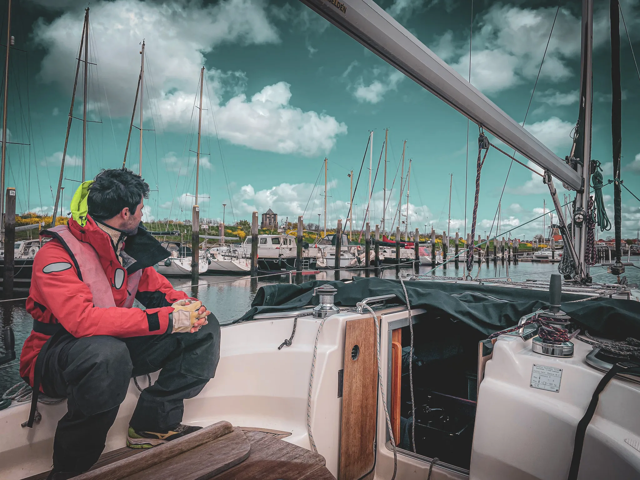 Un marin contemplant le port depuis un voilier, sous un ciel dramatique et des voiles dressées.