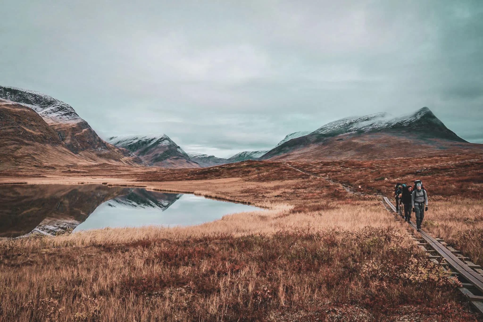 Hikers on a wooden trail, surrounded by mountains and a peaceful lake in Lapland.