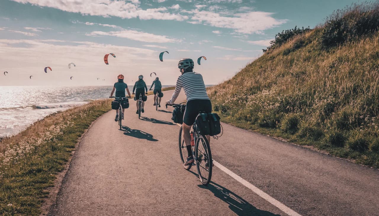 Groep fietsers fietst langs de Zeeuwse kust, met kitesurfers op de achtergrond.