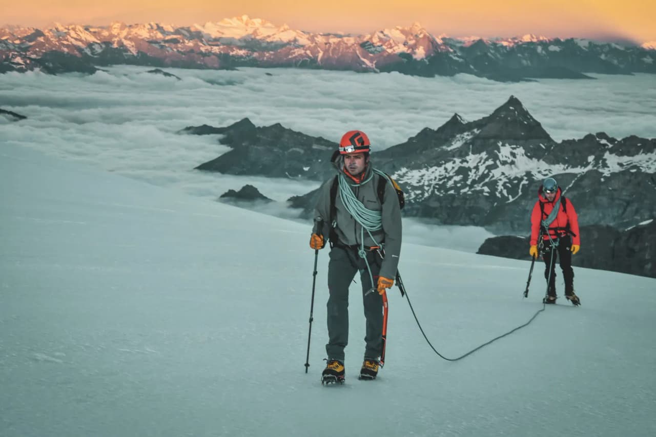 Deux alpinistes progressent sur un glacier, avec un paysage majestueux de montagnes à l'arrière-plan.