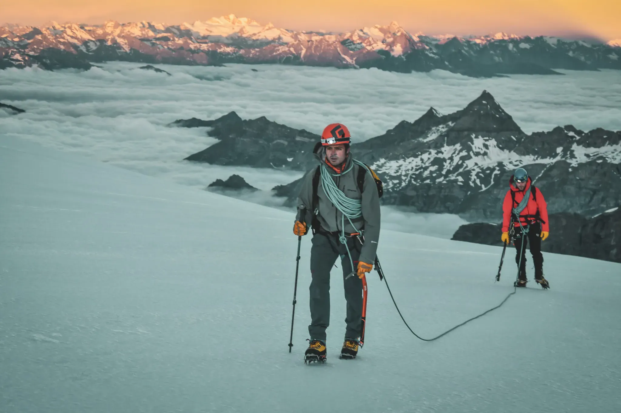 Deux alpinistes progressent sur un glacier, avec un paysage majestueux de montagnes à l'arrière-plan.