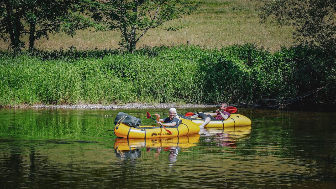 Wandelaars in packrafts drijven rustig op een rivier, omringd door weelderig groen.