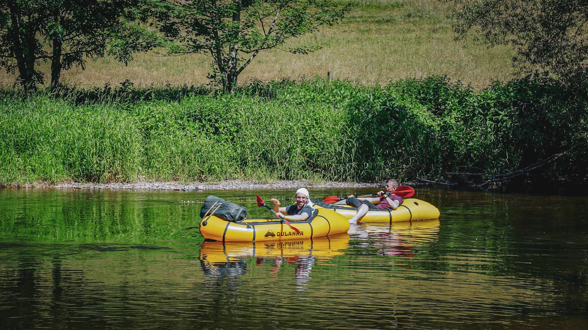 Des randonneurs en packraft flottent paisiblement sur une rivière entourée de verdure luxuriante.