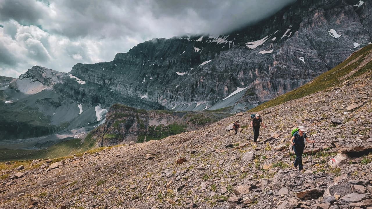 Hikers on an alpine trail, surrounded by majestic mountains and dramatic clouds.