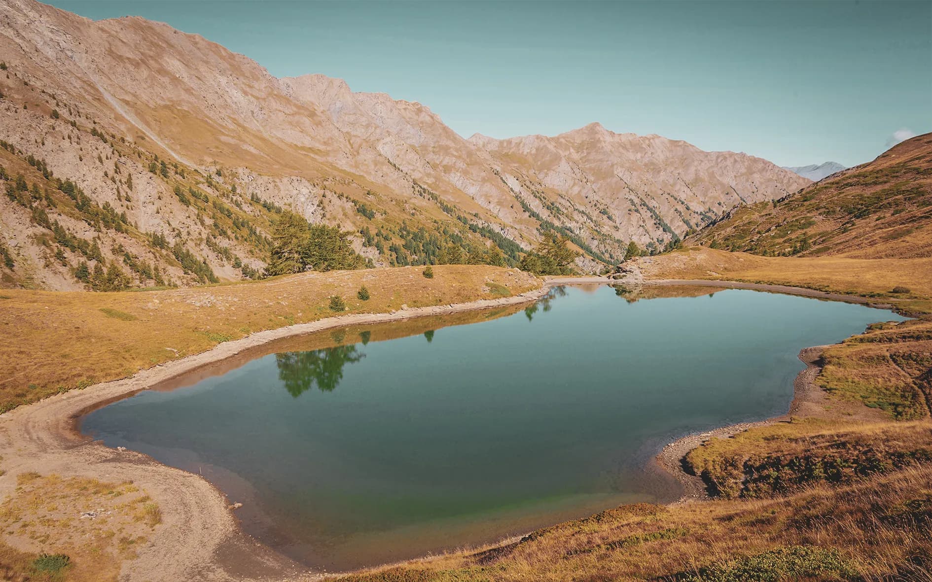 A peaceful lake surrounded by golden mountains, an invitation to escape to the Queyras.