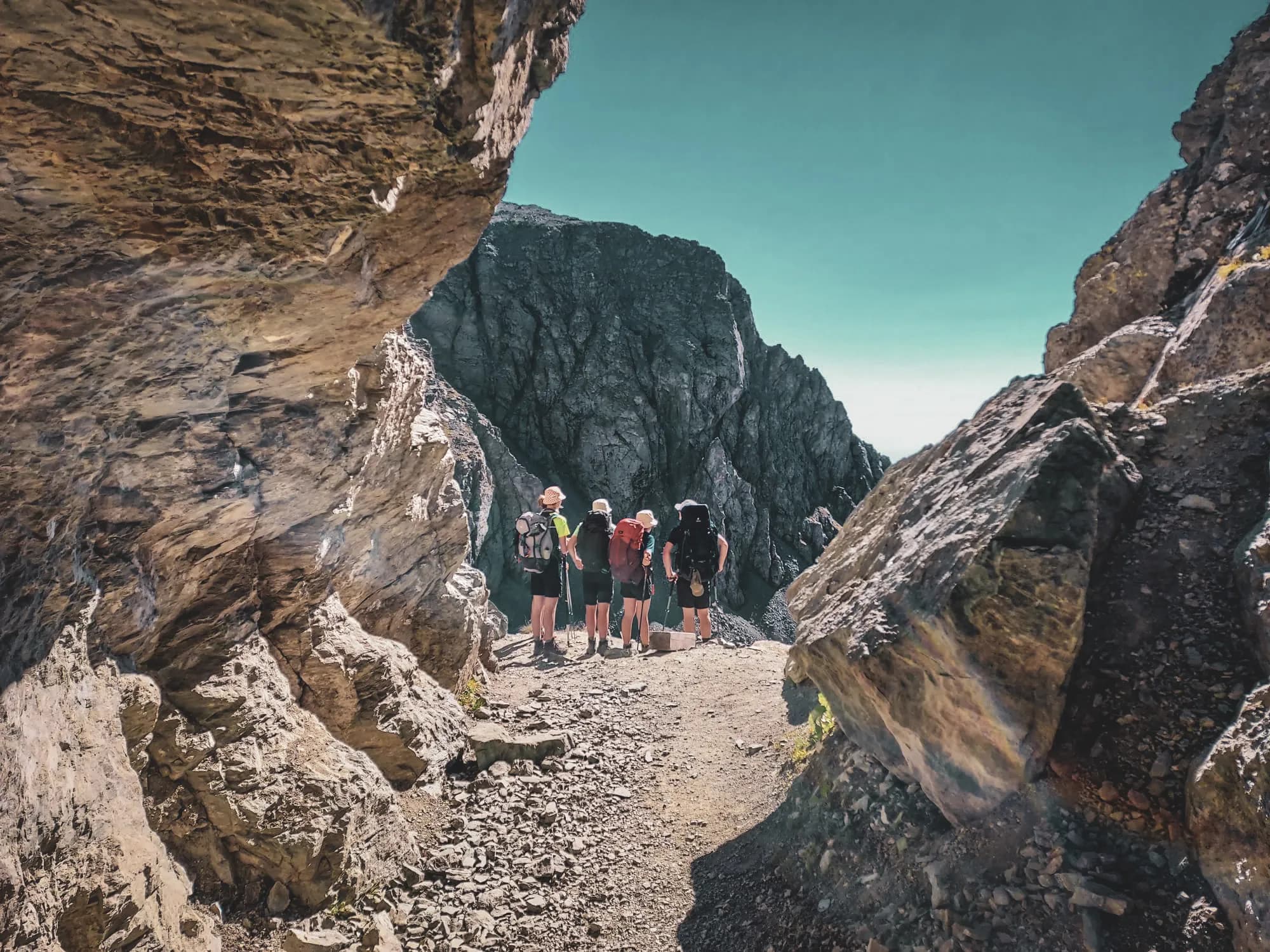 Groupe de randonneurs sur un sentier alpin, entouré de rochers majestueux et ciel bleu.