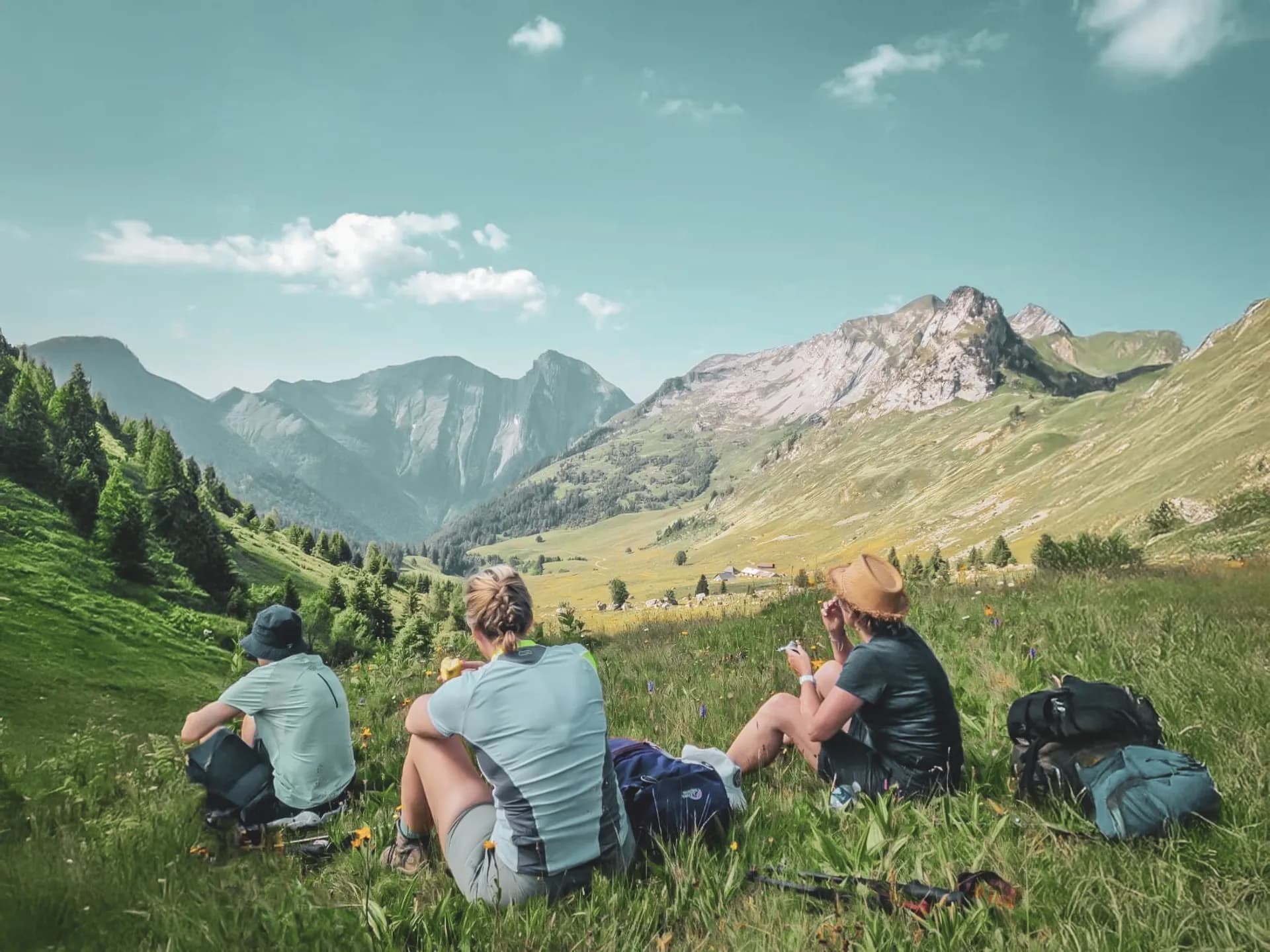 A group of hikers relaxing in a green landscape with majestic mountains in the background.