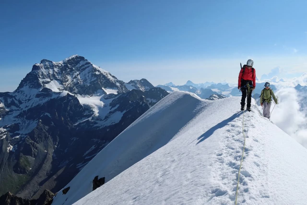 Mountaineers on a snow-covered ridge, facing Mont Blanc, under a blue sky. Alpine adventure!
