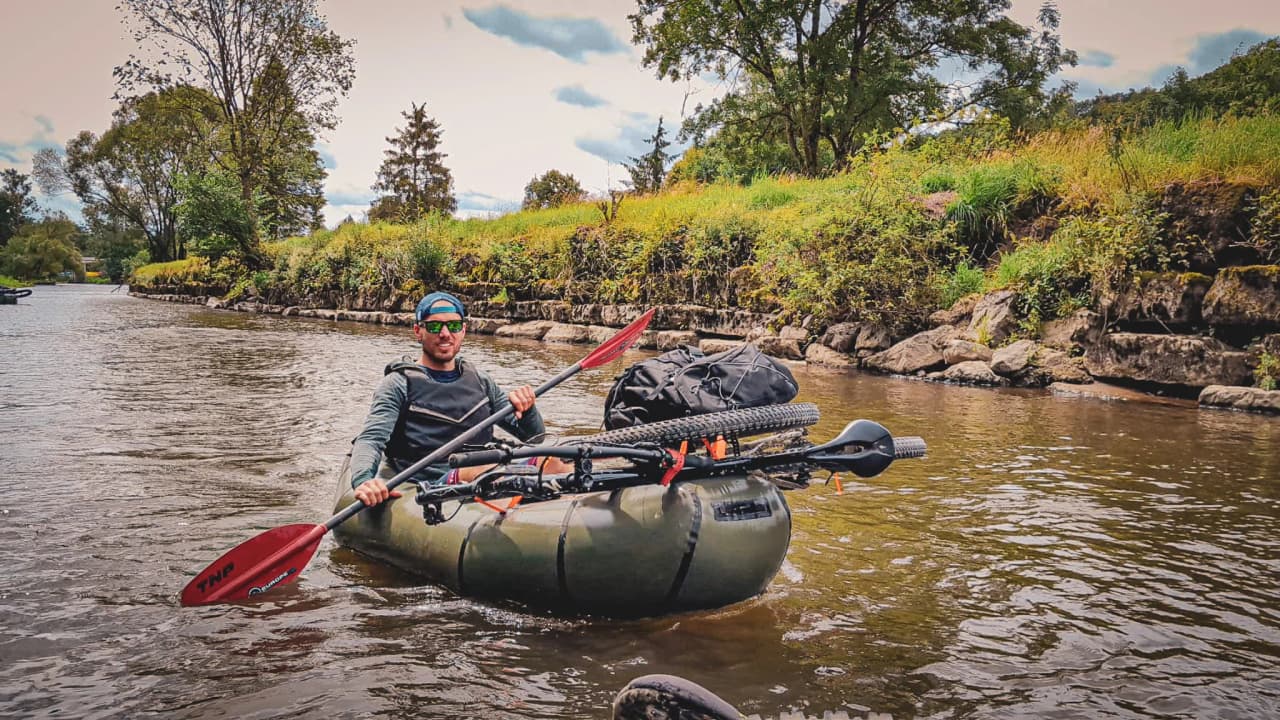 An adventurer paddling through a green valley, kayak and bike ready for exploration.