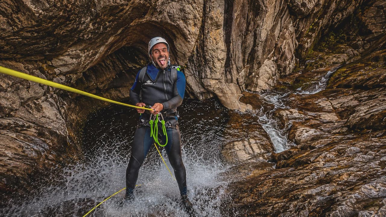 Un aventurier souriant en combinaison, rappelant le long d'une cascade turquoise en pleine nature.