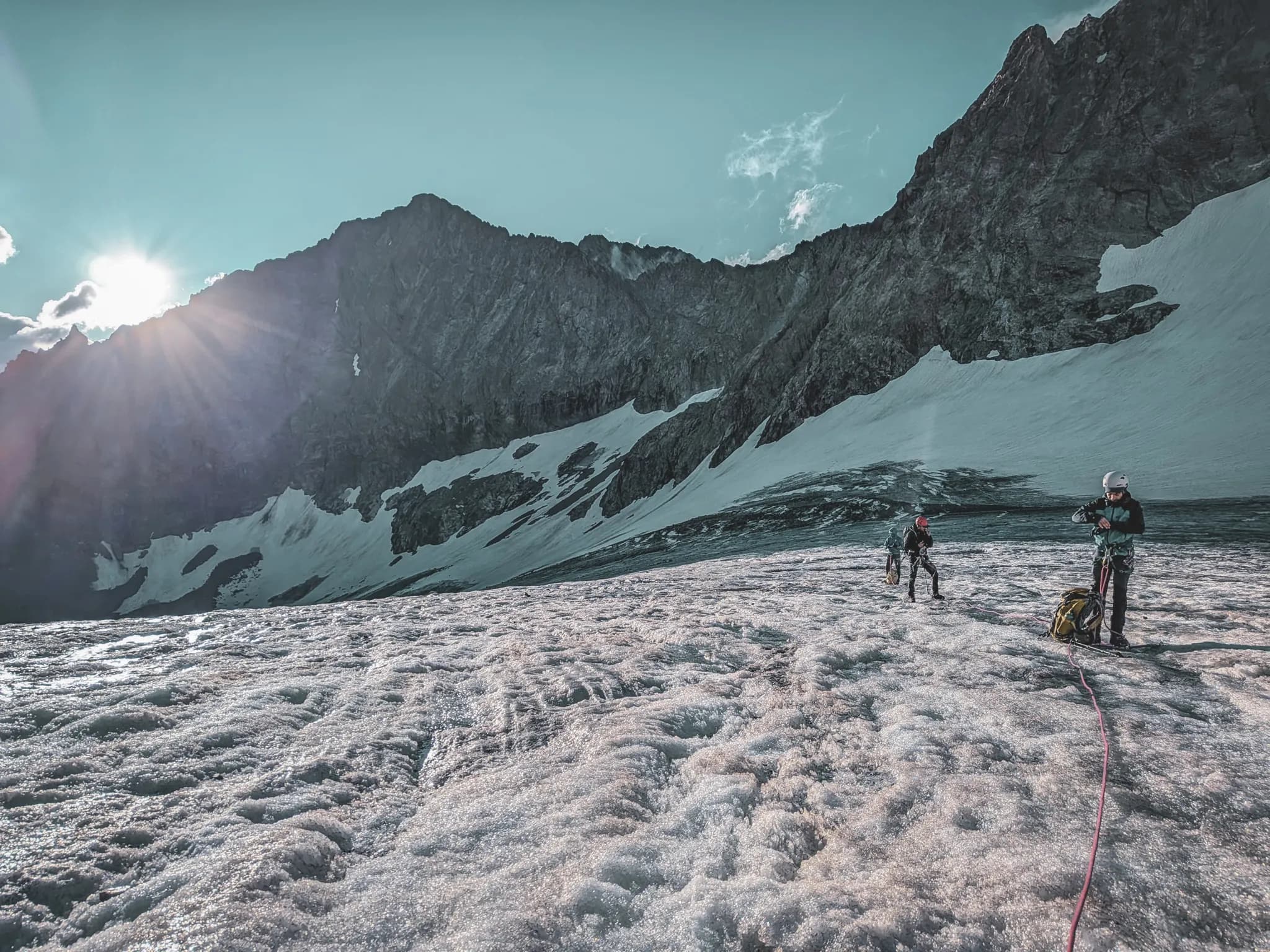 Mountaineers on a sun-drenched glacier, facing the majestic Ecrins mountains.