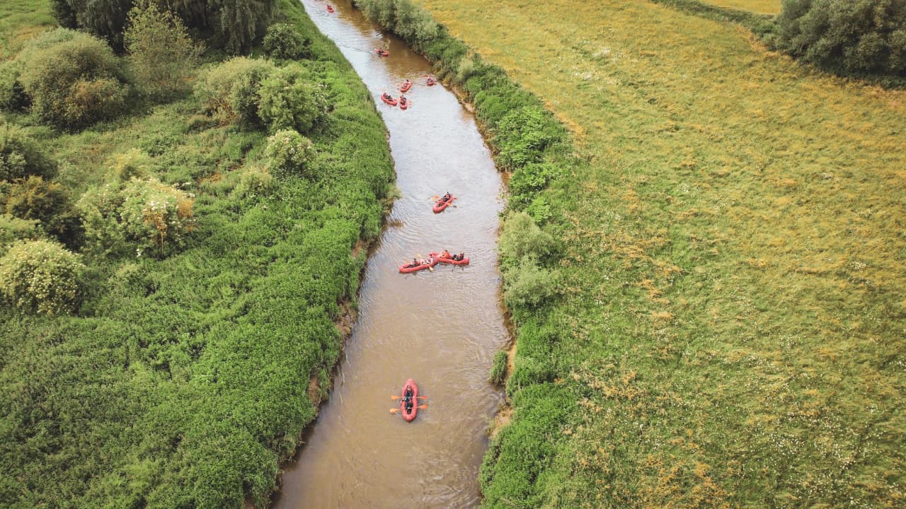 A peaceful river meanders through the greenery, red packrafts gliding on the water, inviting adventure.