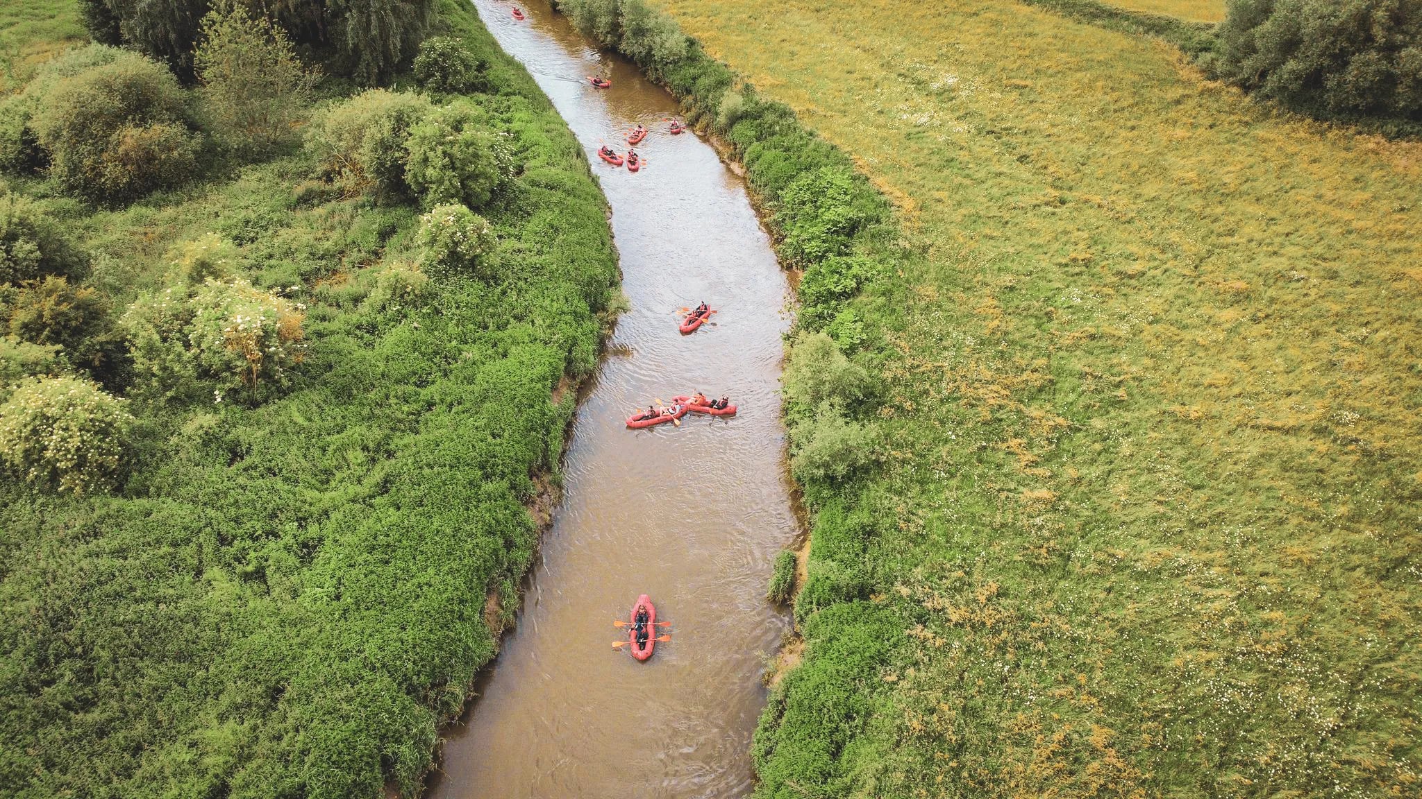 Une paisible rivière serpente entre la verdure, des packrafts rouges glissent sur l'eau, invitant à l'aventure.