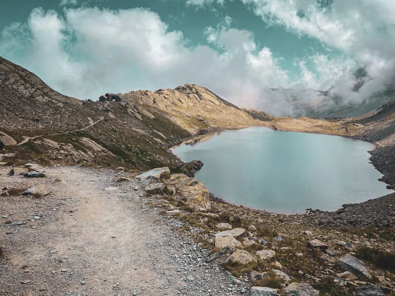 Een rustig meer omringd door bergen, met een kronkelend pad dat uitnodigt om de Alpen te verkennen.