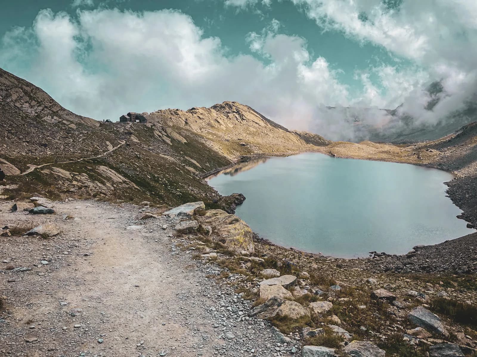 Lac tranquille entouré de montagnes, chemin sinueux invitant à l'exploration alpine.
